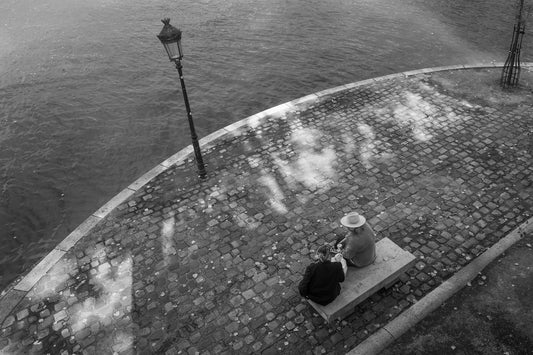 Two people sitting on a bench by a waterfront with a lamp post nearby.